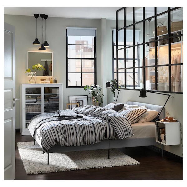 Двуспальная кровать с матрасом и постельными принадлежностями в светлом интерьере спальни.
